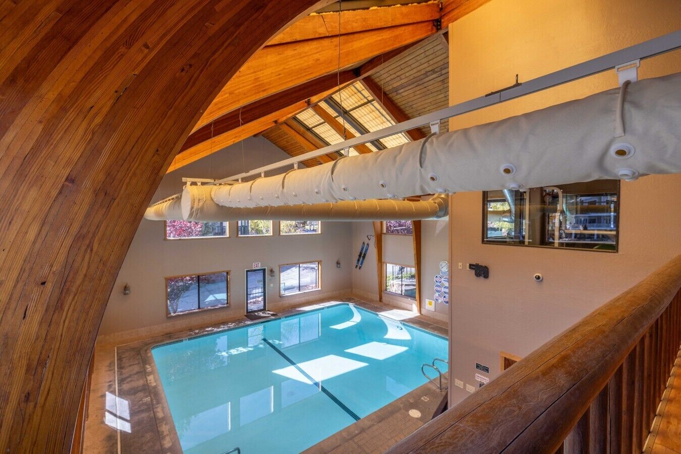 An indoor swimming pool with a glass wall, wooden beams, and a skylight.