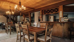 A wooden dining area with a bar, wooden chairs, and a chandelier. - Golden Hour | Jacuzzi, Sauna, Pool, Tennis, Gated! (Big Bear Lake)