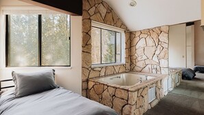 A bedroom with a large window, a stone wall, and a bathtub. - Golden Hour | Jacuzzi, Sauna, Pool, Tennis, Gated! (Big Bear Lake)
