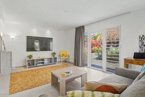 A modern living room with a flat-screen TV, a sofa, a coffee table, a bookshelf, and a sliding glass door leading to an outdoor area.