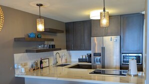 Une cuisine moderne dotée d’un îlot central, de meubles de couleur sombre et de luminaires suspendus.