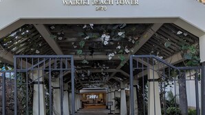 L'entrée de la tour Waikiki Beach se distingue par un chemin pavé de pierres, des portails en métal et un panneau indiquant que l'entrée par l'ascenseur est à utiliser après 17h00.
