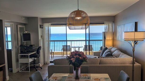 Une chambre d’hôtel équipée d’une table à manger, de chaises, d’un canapé, d’une télévision, d’un bureau et offrant une vue sur la mer.