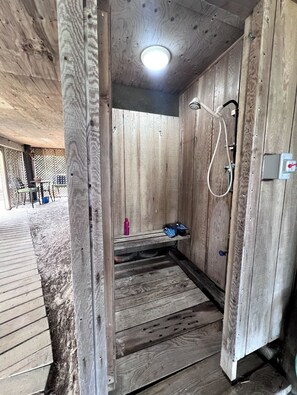 Ein Holzinnenraum mit Dusche, einer Bank und einem kleinen Tisch mit Gegenständen darauf.