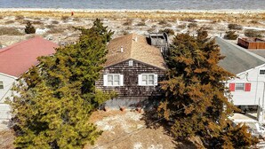 A coastal house with a red roof, surrounded by trees and a beach in the background. - Beach Front. The Plum Pad. Sunset, Surf & 70s Soul (Milton)