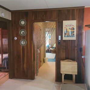 Ein Holzinnenraum mit einer zur einem Zimmer führenden Tür, einem Poster an der Wand und einem kleinen Tisch.