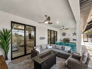 Une terrasse extérieure avec un canapé, une table, des ventilateurs de plafond et un espace barbecue.