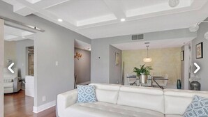 Un salon moderne avec un canapé blanc, un coin repas comprenant une table et des chaises, et un couloir menant à une autre pièce.