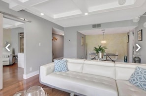 A modern living room with a white sofa, a dining area with a table and chairs, and a hallway leading to another room. - Serene Golf Course Escape - Upscale 2BR/2BA - Gated Community Living (Boca Raton)