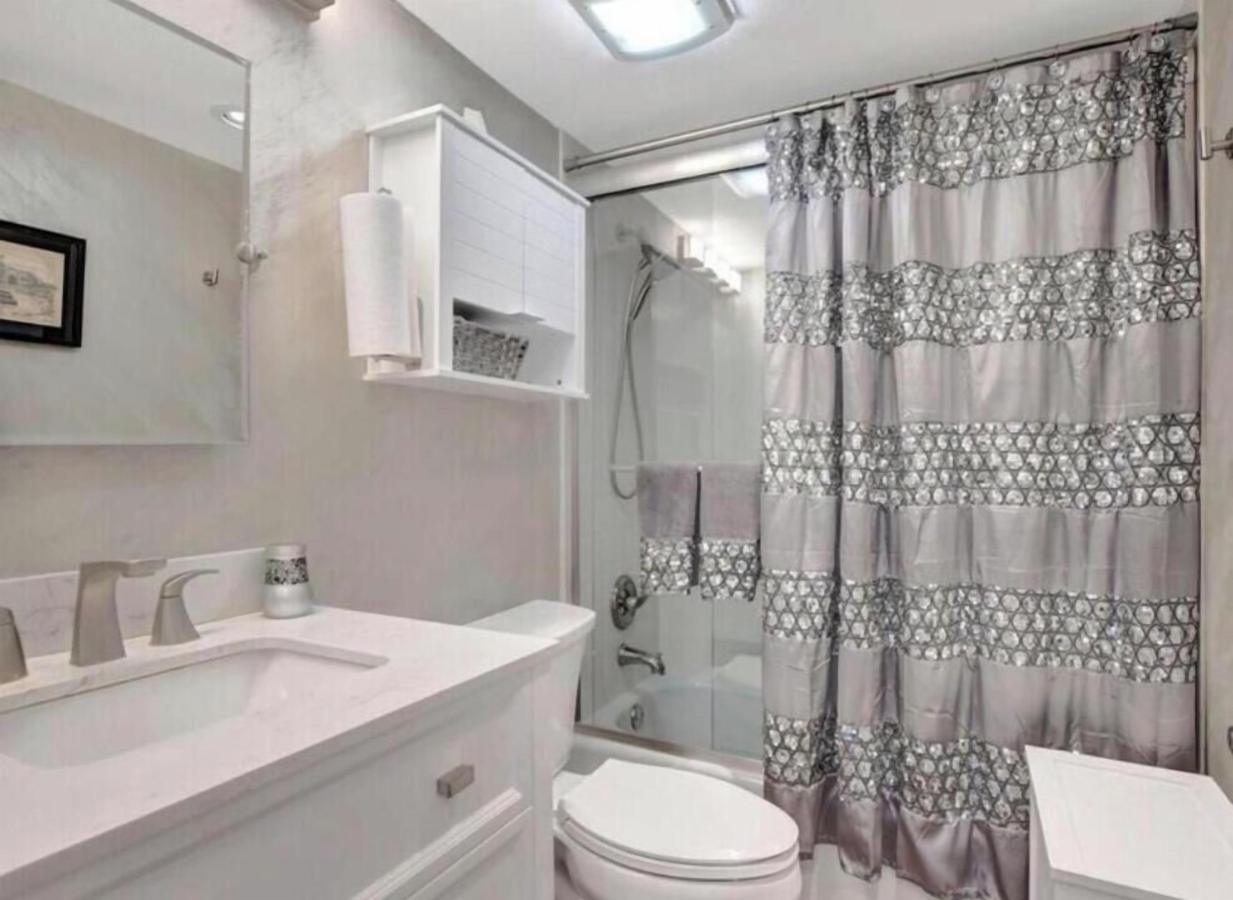 Une salle de bain avec un rideau de douche, des toilettes, un lavabo avec un miroir et un porte-serviettes.
