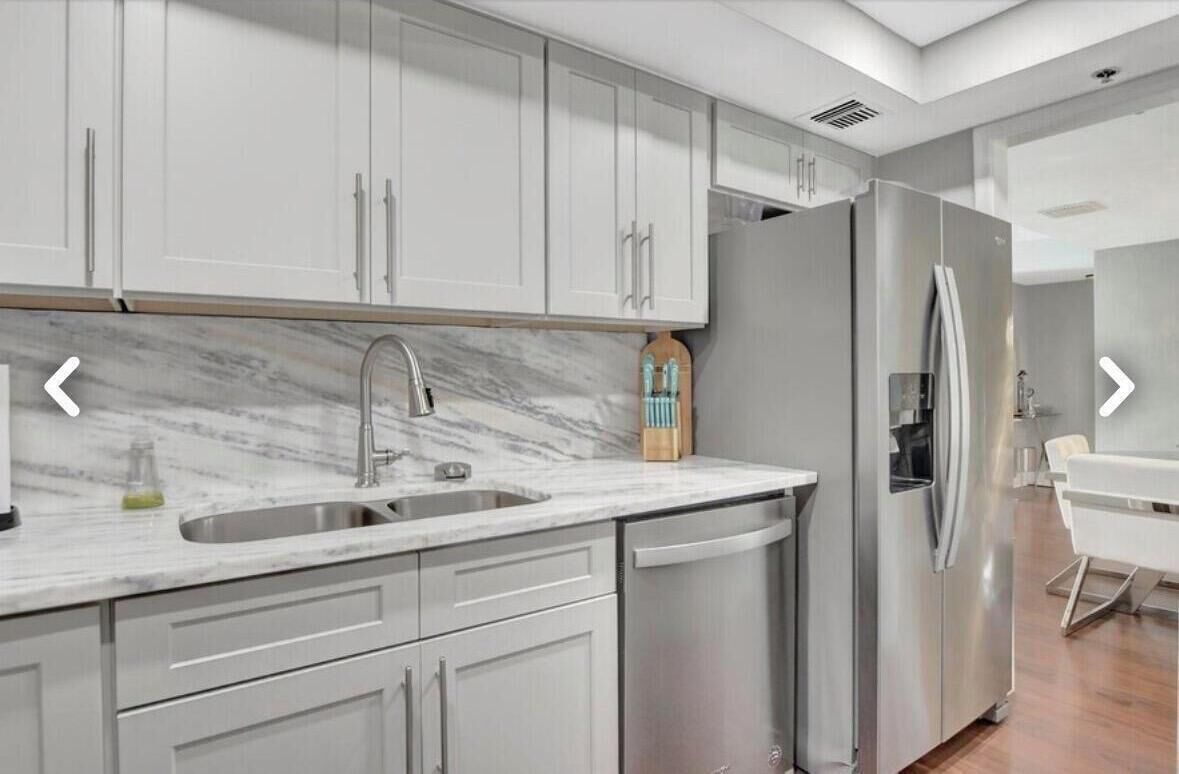 A modern kitchen with white cabinets, a marble countertop, a stainless steel refrigerator, and a dishwasher.