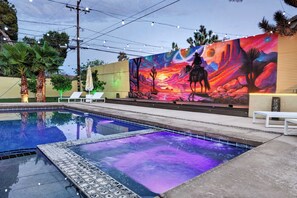 A swimming pool with a colorful mural on the adjacent wall, surrounded by palm trees and lounge chairs. - Desert Gold House By Homestead Modern (Yucca Valley)