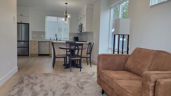 A modern kitchen with a dining area, a sofa, and a large window.