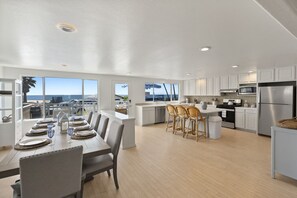 A modern kitchen with white cabinets, stainless steel appliances, and a dining area with a view of the ocean. - Cute Beach Cottage, Walk to Beach & Restaurants (Oceanside)