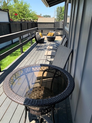 En overdækket terrasse med et bord i glas og fletstole.