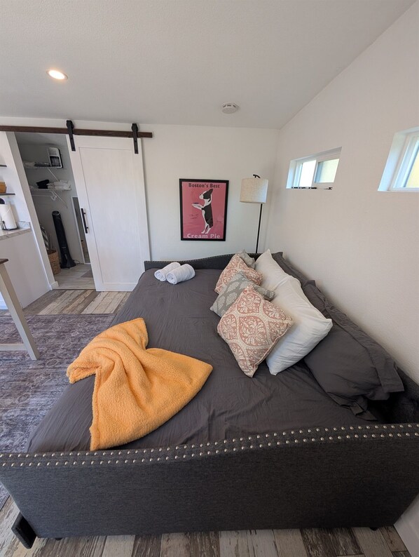 A bedroom with a bed, pillows, a blanket, a poster, a lamp, and a view of the hallway.