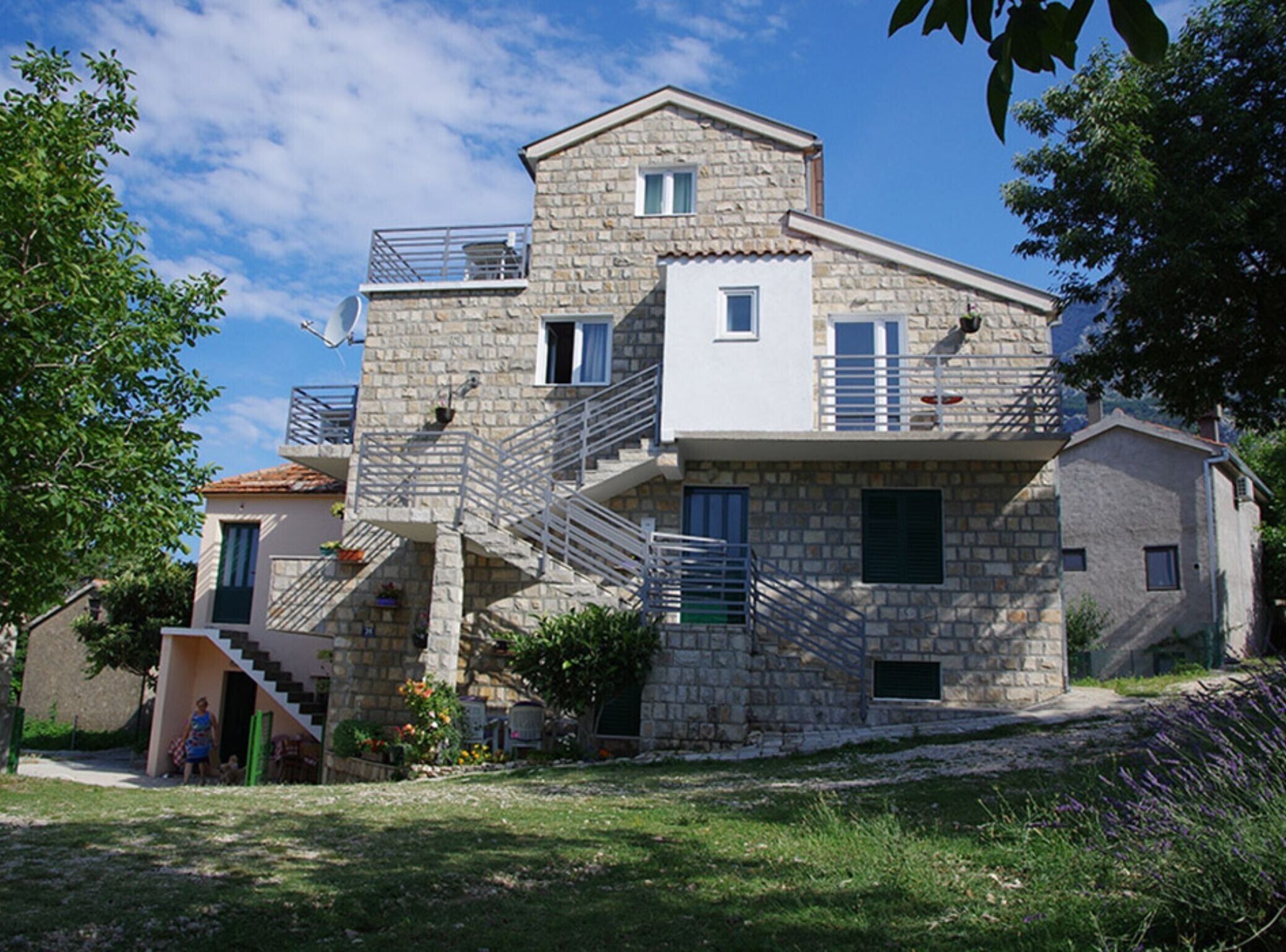 A stone building with a staircase leading to a balcony, surrounded by greenery.