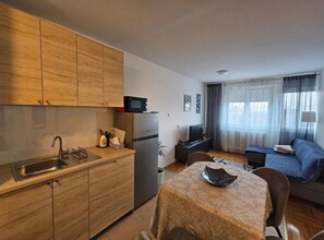 A compact living space with a kitchenette, a dining area with a table and chairs, a sofa, and a television. - Apartman FITT - Apartman (Zagreb)