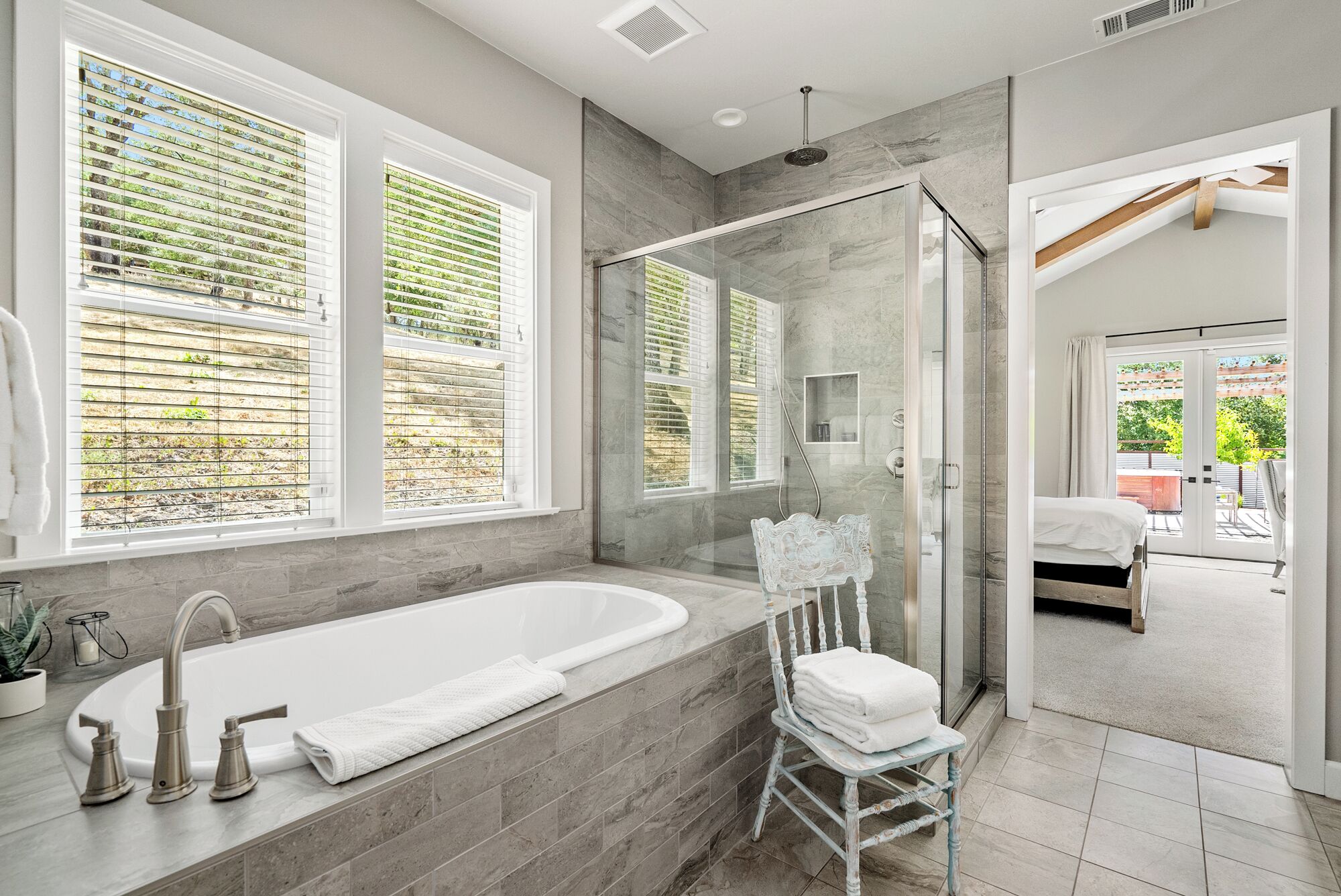 A modern bathroom with a large bathtub, a glass-enclosed shower, and a view of the outdoors through large windows.