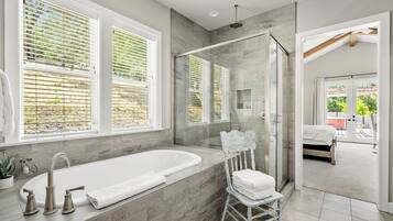 A modern bathroom with a large bathtub, a glass-enclosed shower, and a view of the outdoors through large windows.