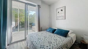 A bedroom with a bed, a large sliding glass door, a framed artwork on the wall, and a small bedside table. - Maisonette duplex in residence with swimming pool facing the golf course (La Grande-Motte)