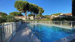 Una piscina con una valla blanca, una escalera y árboles al fondo.