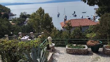 A coastal view with a stone-paved terrace, a table with chairs, and a statue.
