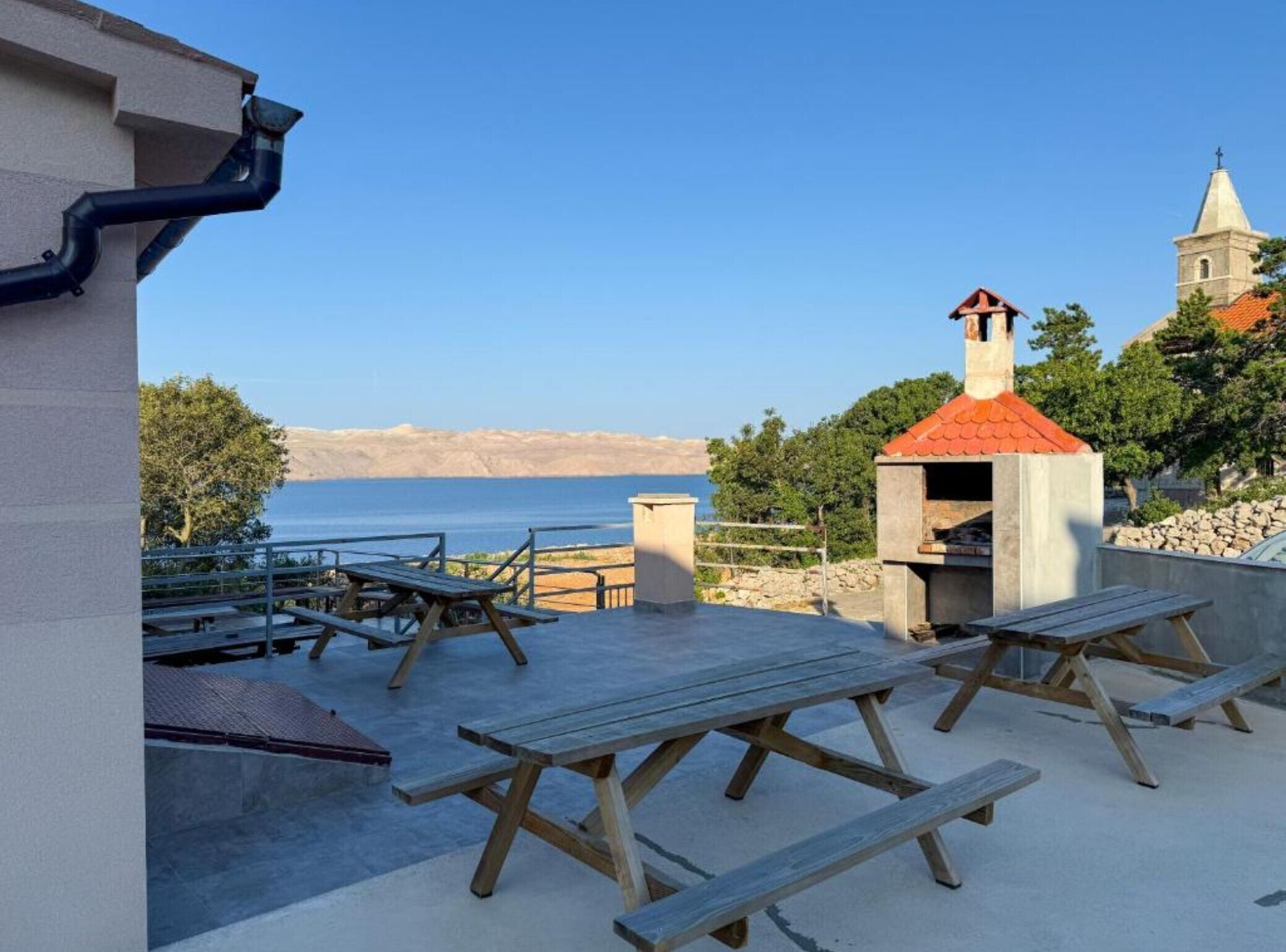 Un patio al aire libre con mesas de picnic, una parrilla y vista al mar.