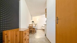 Een smalle gang met een houten dressoir, een stoel, een bed en een bureau met een computer.