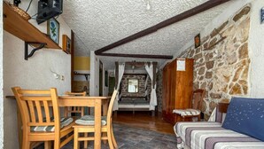 A cozy room with a wooden dining table, chairs, a sofa, and a stone wall. - Fischer Fritz Apartments - Studio Apartment (Betina)