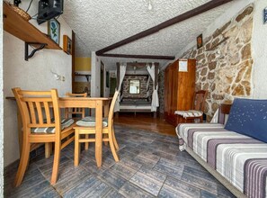Ein gemütliches Zimmer mit Holztisch, Stühlen, einer Couch und einer Steinwand.