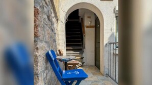 A narrow outdoor corridor with stone walls, a blue folding chair, and a small table. - Fischer Fritz Apartments - Studio Apartment (Betina)