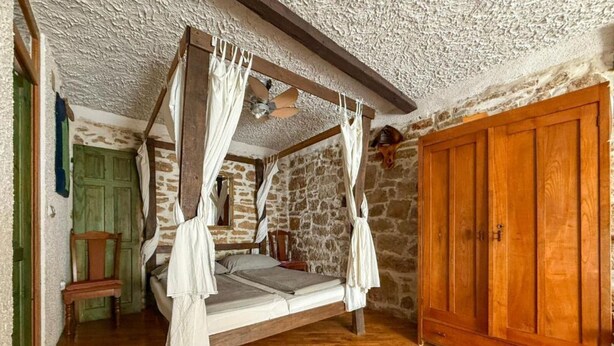 A four-poster bed with a canopy, a wooden wardrobe, and a stone wall. - Fischer Fritz Apartments - Studio Apartment (Betina)