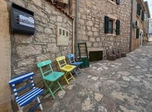 A stone building with a rustic exterior, a small outdoor seating area with colorful chairs, and a utility box mounted on the wall. - Fischer Fritz Apartments - Classic One Bedroom Apartment (Betina)