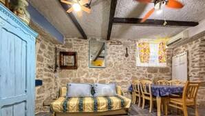 Une pièce rustique avec un mur en pierre, un lit en bois avec une literie à motifs, une table à manger avec des chaises et un ventilateur de plafond.