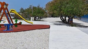 Ein Spielplatz mit Rutsche und Schaukeln, einem gepflasterten Weg und Bäumen.