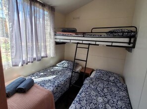 A dormitory room with bunk beds, a window with curtains, and a small table with a rolled-up blanket. - Mobile Home Nalani- Two Bedroom Mobile Home (Razanac)