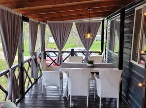 A covered outdoor seating area with a table and chairs, a hanging light fixture, and a view of parked cars and greenery. - Mobile Home Nalani- Two Bedroom Mobile Home (Razanac)