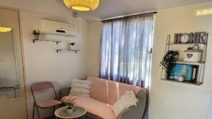 Ein gemütliches Wohnzimmer mit einer Couch, einem kleinen Tisch und einem Sessel. Ein Regal mit Dekoration und eine Wanduhr sind ebenfalls vorhanden.