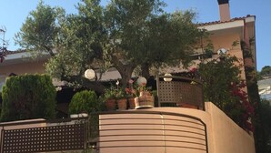 A building with a curved balcony, potted plants, and a tree. - Magic mola (Chalkidiki)