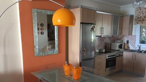 A modern kitchen with a glass dining table, stainless steel appliances, and orange walls. - Magic mola (Chalkidiki)