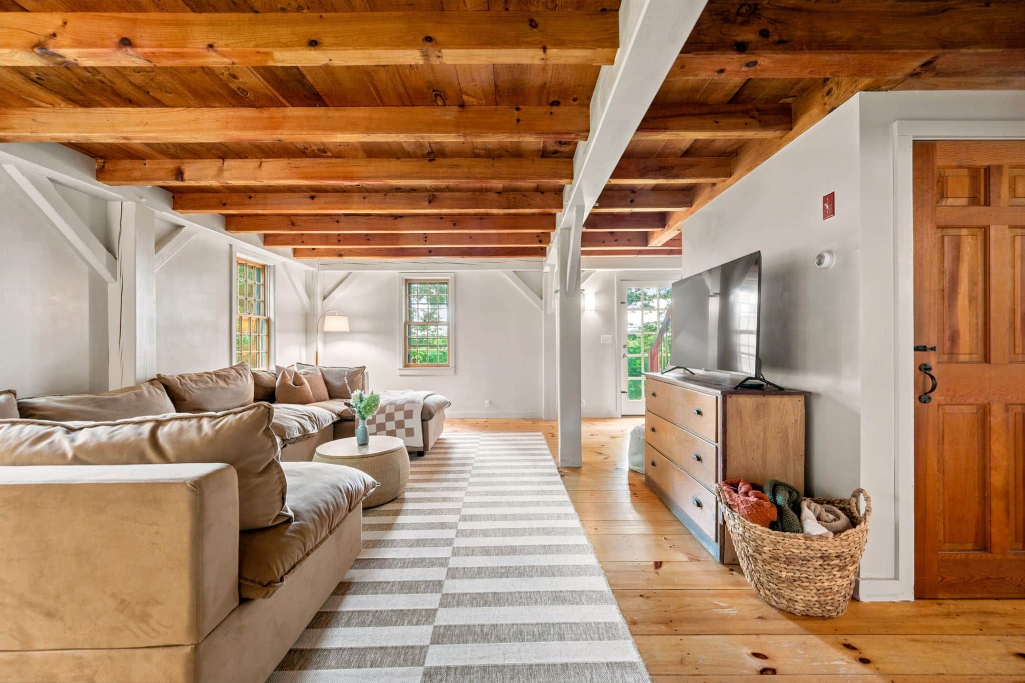 A spacious living room with a wooden ceiling, a sofa set, a television, and a view of the outdoors.