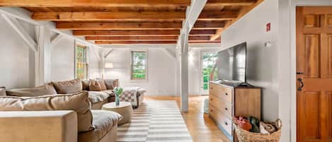 A spacious living room with a wooden ceiling, a sofa set, a television, and a view of the outdoors.