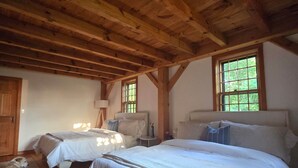 Ein Schlafzimmer mit zwei Betten, Holzbalken, einem Deckenventilator und einem Fenster mit Blick auf Bäume.