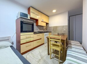 A compact kitchen with a microwave, oven, and sink, a small dining table with chairs, and a bed with a striped blanket. - Capo & Nemo Apartments Vodice (Vodice)