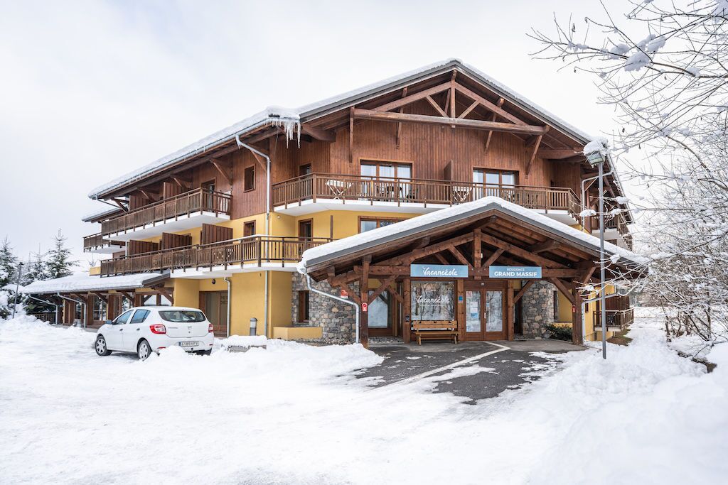Ein mehrstöckiges Holzhaus mit Balkonen, einem überdachten Eingang und einem Schild mit der Aufschrift 'Vacanzele Grand Massif'.