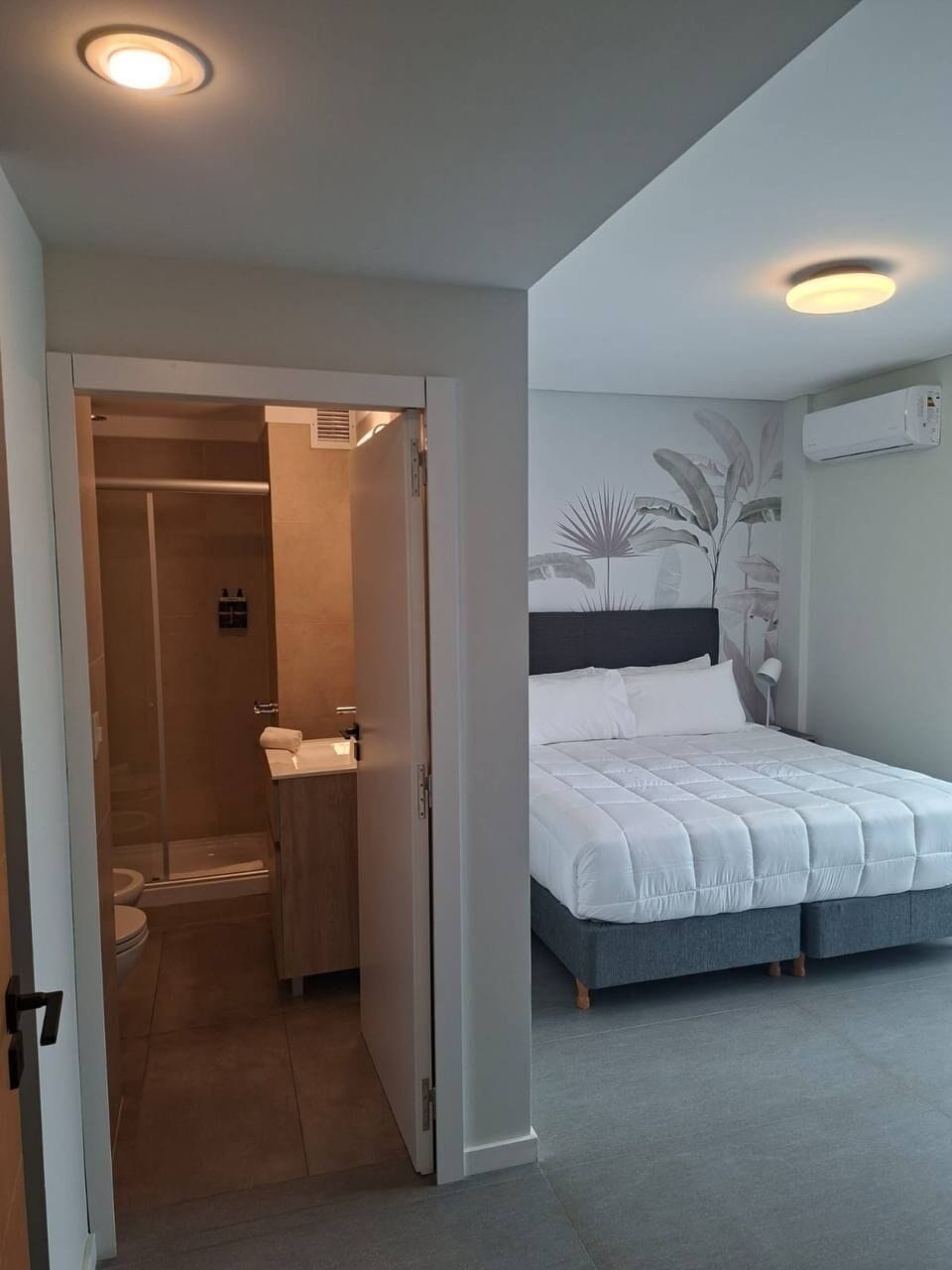 Un dormitorio con cama, un baño con ducha y una puerta que da a otra habitación.