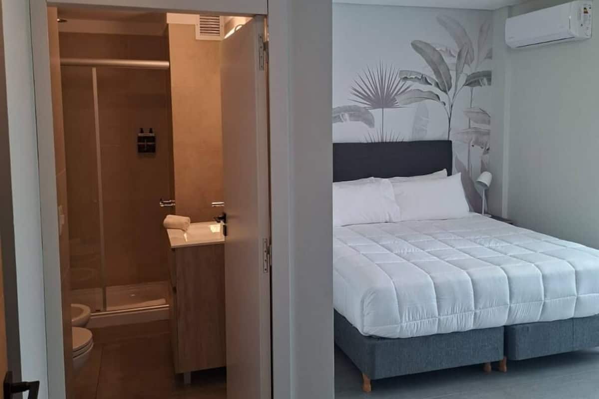 A bedroom with a bed, a bathroom with a shower, and a door leading to another room.