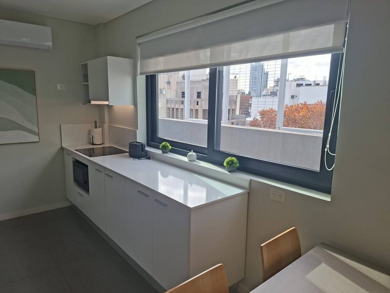 A modern kitchen with a large window, white cabinetry, and a small dining area with a table and chairs.