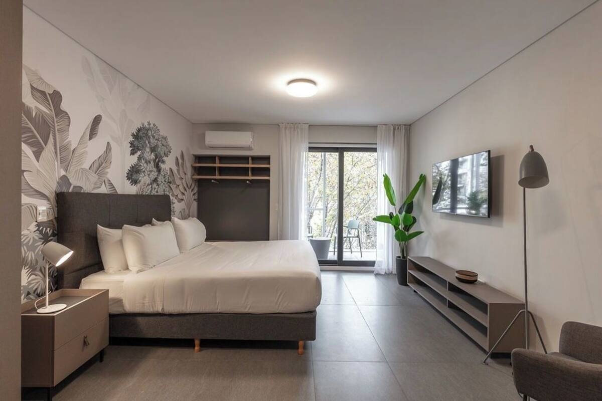 A modern bedroom with a bed, bedside table, lamp, TV, and a large window.